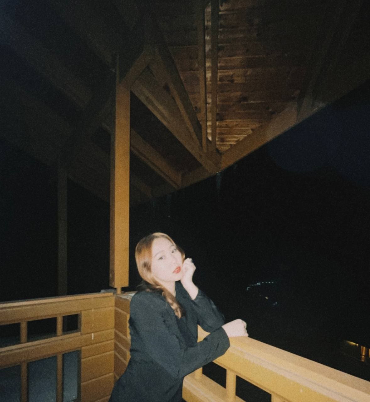 Elegant woman standing on a wooden balcony at night, showcasing fashion and style.